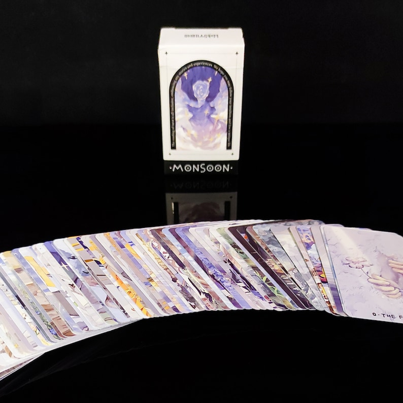 May include: A deck of cards with a white box featuring a purple and blue illustration of a person in the clouds. The box has the text "MONSOON" on the front.