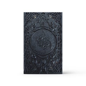 May include: A dark grey rectangular box with detailed embossed patterns. The box has a central circular emblem with a Celtic knot design, surrounded by ornate patterns and scrollwork. The overall aesthetic is gothic and decorative.