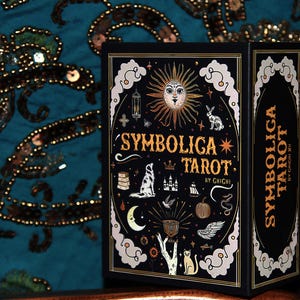 Puede incluir: Una caja negra de cartas del tarot con detalles dorados y el texto "Symbolica Tarot". La caja presenta ilustraciones de un sol, un conejo, un perro y otros símbolos místicos. La caja está sobre un fondo turquesa.