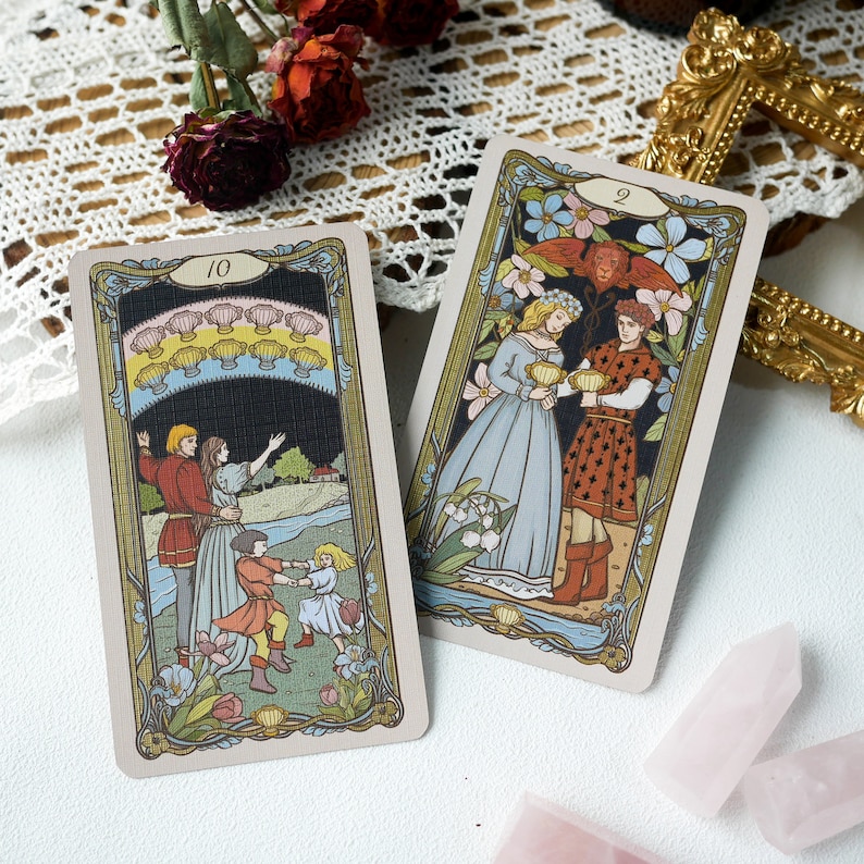 May include: Two tarot cards, one with the number 10 and the other with the number 2. The card with the number 10 depicts a family of four with a dark blue sky and a rainbow of seashells above them. The card with the number 2 depicts a couple in medieval clothing holding cups, with a floral background.