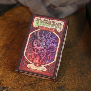 May include: A rectangular card game box titled Sons of the Pantheon Cthulhu Mythos Cards. The box features a dark red and purple illustration of a multi-eyed, tentacled creature within an ornate frame, with green and white text on the front.