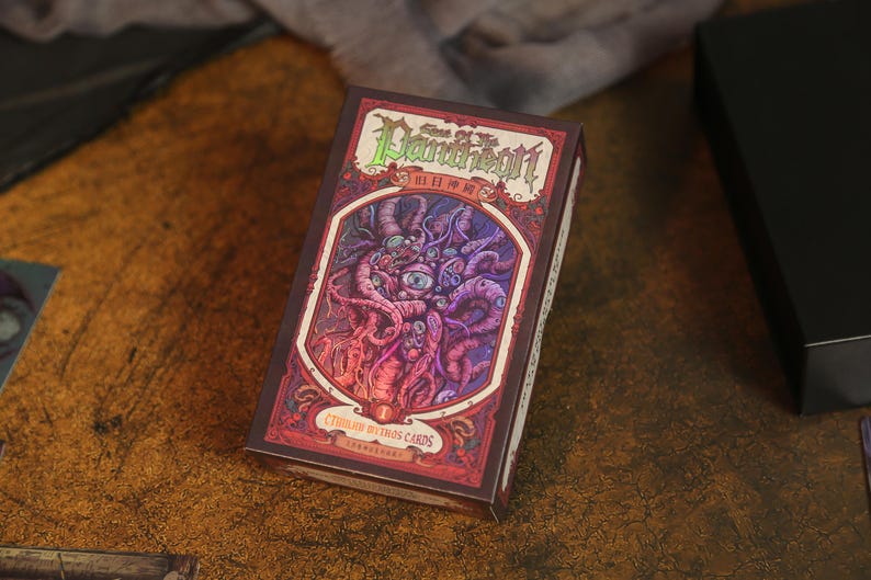 May include: A rectangular card game box titled Sons of the Pantheon Cthulhu Mythos Cards. The box features a dark red and purple illustration of a multi-eyed, tentacled creature within an ornate frame, with green and white text on the front.
