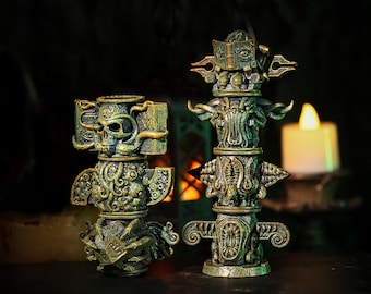 May include: Two detailed, antique-style totem statues with a weathered, bronze-green finish. One features a skull, the other a book, both with intricate carvings. A candle glows in the background, enhancing the mystical theme.