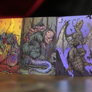 May include: Three rectangular trading cards featuring detailed, colorful illustrations of monstrous creatures. The left card shows a yellow-toned insectoid beast, the center card depicts a green, multi-eyed creature, and the right card shows a winged, skeletal monster on a purple background.