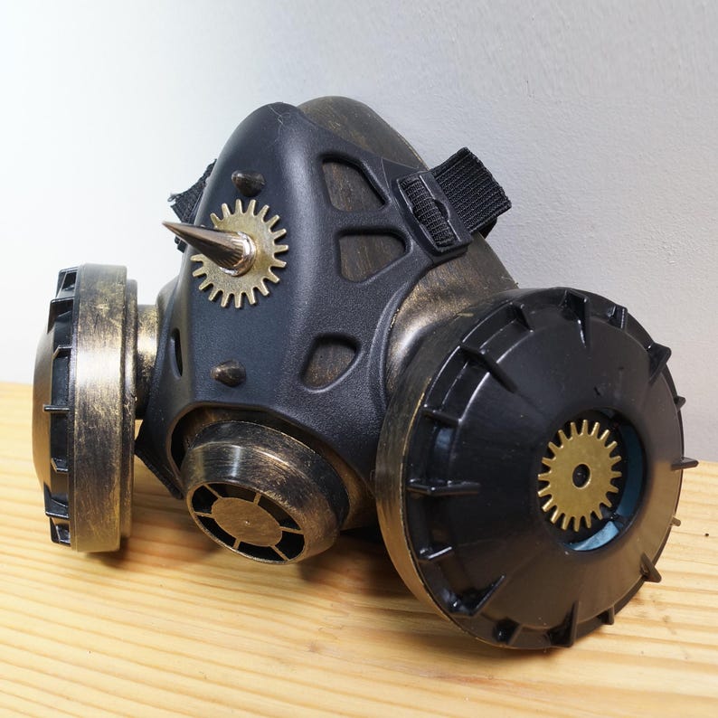 May include: A black and gold steampunk-style gas mask with gears and a spike on the front. The mask has two round, black filters on the sides.