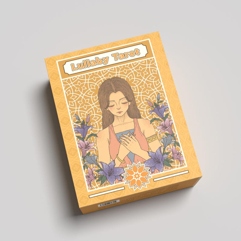 K&ouml;nnte beinhalten: Eine Tarotkartenbox mit dem Titel "Lullaby Tarot" in einem dekorativen Banner. Die Box zeigt eine Illustration einer Frau, die von Blumen umgeben ist. Das Farbschema ist haupts&auml;chlich gelb, mit Akzenten in Rosa, Blau und Lila.