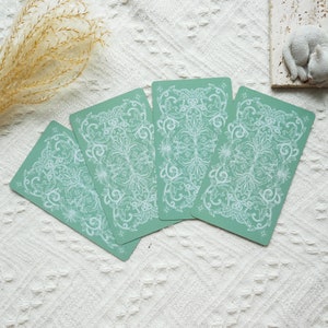 May include: Four green tarot cards with white floral designs. The cards are arranged in a fan shape.