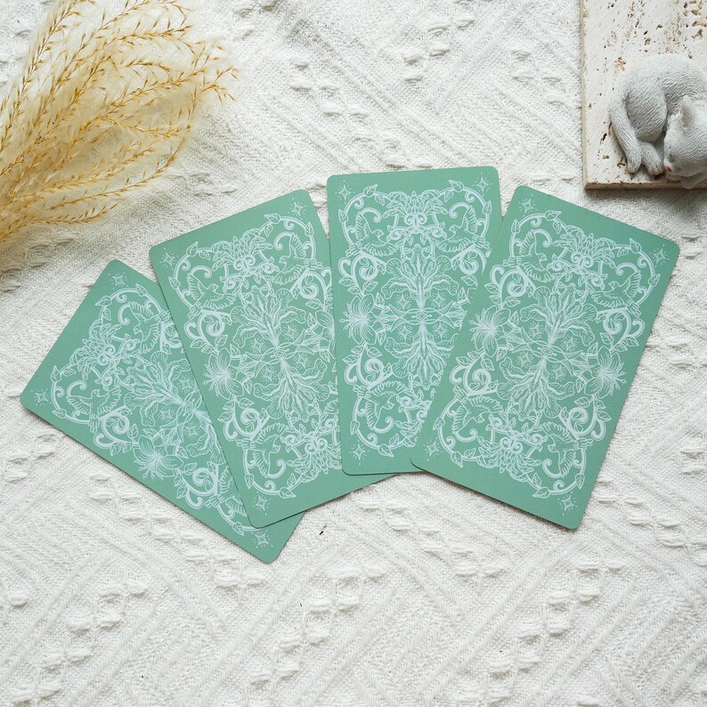 May include: Four green tarot cards with white floral designs. The cards are arranged in a fan shape.