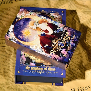 Puede incluir: Una baraja de cartas del tarot "The Radiant Essence". La caja y los dorsos de las cartas son de color azul marino con dise&ntilde;os florales y celestiales. Las caras de las cartas presentan a una mujer con un vestido rojo dentro de una luna creciente y una estrella.