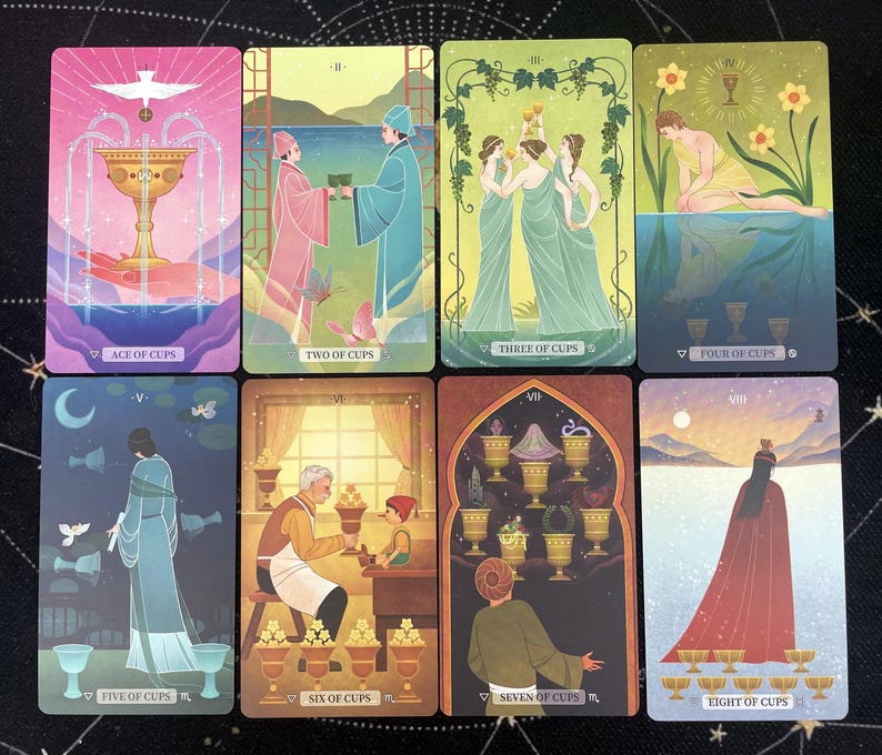K&ouml;nnte beinhalten: Acht Tarotkarten mit farbenfrohen Illustrationen. Jede Karte zeigt eine andere Szene mit Figuren, Bechern und Symbolen. Die Karten sind mit r&ouml;mischen Ziffern und Titeln wie "Ace of Cups" und "Two of Cups" beschriftet. Die Karten liegen auf einer dunklen Oberfl&auml;che.