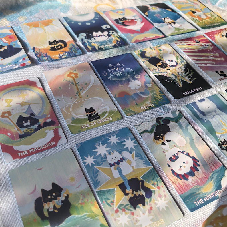 K&ouml;nnte beinhalten: Eine Sammlung von Tarotkarten mit Illustrationen von Katzen in verschiedenen Posen und Umgebungen. Jede Karte zeigt einen spezifischen Titel wie The Sun, The Moon, The Magician, Ace of Wands, Death, Judgement, The Star und The Hanged Man.