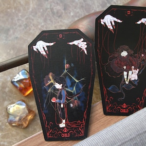 May include: Two coffin-shaped cards with black backgrounds and red accents. Each card features the number 13, the word CHILD, and an illustration of a child being controlled by puppet strings held by white hands with red fingernails.