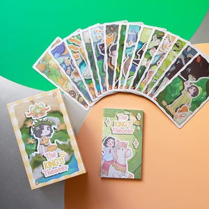 May include: A collection of illustrated cards and two small boxes, all featuring a whimsical design. The cards are fanned out, showcasing various scenes with cartoon characters and the text "The King's Theater". The boxes also display similar artwork.