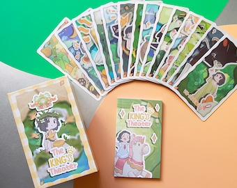May include: A collection of illustrated cards and two small boxes, all featuring a whimsical design. The cards are fanned out, showcasing various scenes with cartoon characters and the text "The King's Theater". The boxes also display similar artwork.