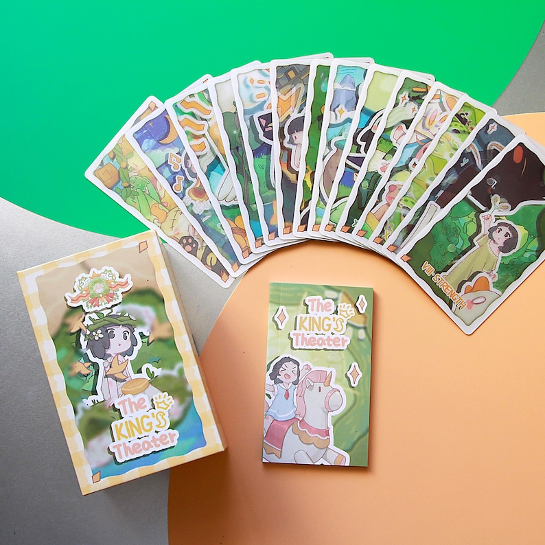 May include: A collection of illustrated cards and two small boxes, all featuring a whimsical design. The cards are fanned out, showcasing various scenes with cartoon characters and the text "The King's Theater". The boxes also display similar artwork.