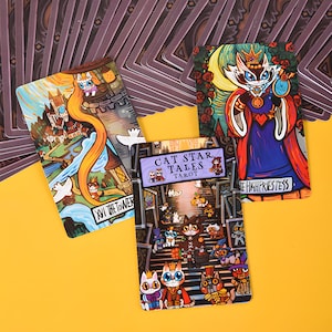 May include: A tarot card deck featuring whimsical cat illustrations. The cards showcase colorful artwork with titles like "The Tower" and "The High Priestess." The deck is titled "Cat Star Tales Tarot."