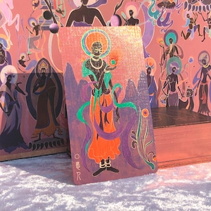 May include: A tarot card featuring a stylized figure with a halo, wearing orange and purple robes, holding a flame. The card has a pink background with other figures and a mountain range. The card is part of a deck.