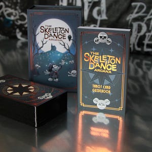 Peut inclure: Un jeu de cartes de tarot intitulé "The Skeleton Dance Arcana". L'ensemble comprend une boîte, un guide et un jeu de cartes. La boîte et le guide présentent des illustrations d'un personnage de dessin animé, de crânes et d'une pleine lune. Les cartes ont un fond noir avec un motif d'étoile.