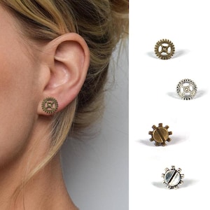 Peut inclure: Une paire de boucles d'oreilles en forme d'engrenage argentées et bronze. Les boucles d'oreilles sont petites et délicates, et elles seraient un excellent cadeau pour un fan de steampunk.