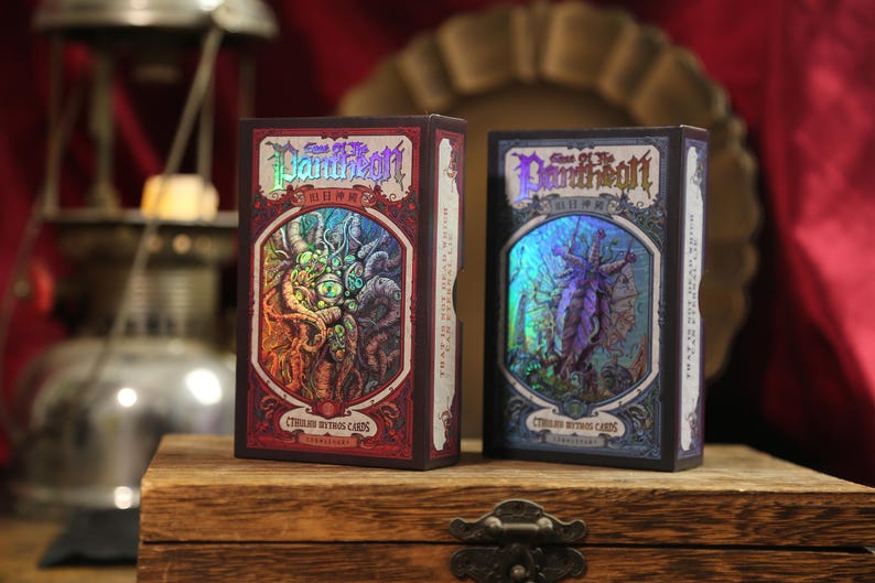 May include: Two rectangular card game boxes titled Call of the Pantheon Cthulhu Mythos Cards. The left box is red with a holographic illustration of a multi-eyed creature. The right box is blue with a holographic illustration of a winged figure.