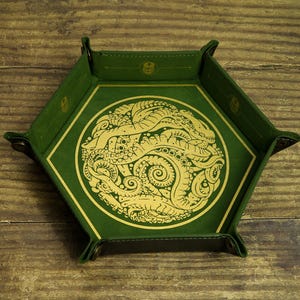 Può includere: Un vassoio da gioco in pelle verde con un disegno dorato di un polpo. Il vassoio è di forma esagonale e ha un bordo rialzato.