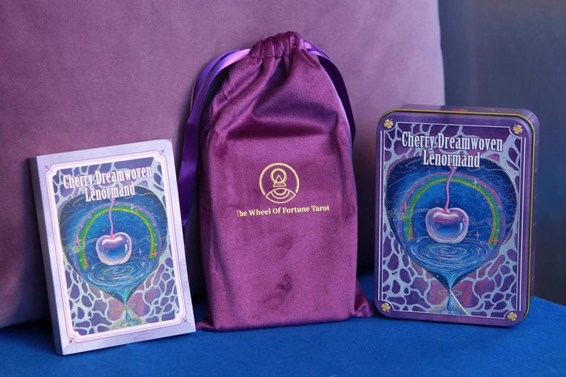 May include: A deck of Cherry Dreamwoven Lenormand cards in a rectangular box, a purple velvet drawstring pouch with a gold logo reading The Wheel Of Fortune Tarot, and a matching rectangular metal tin featuring a cherry and rainbow illustration.