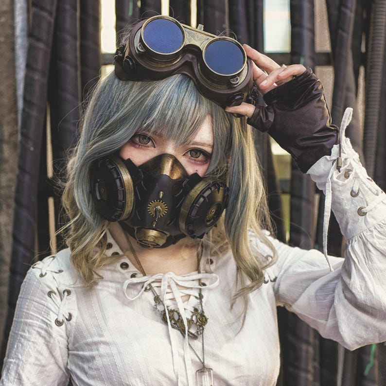 May include: A woman wearing a white blouse with a lace-up detail, a steampunk-style gas mask with gears and brass accents, and goggles with blue lenses. Her hair is styled in a short, choppy cut with blue and blonde highlights.