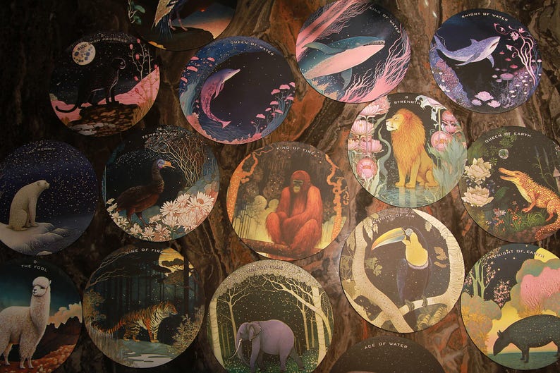May include: A collection of circular art prints featuring various animals and celestial elements. Each print showcases a unique scene, including a lion, whale, and elephant, with vibrant colors and intricate details. The prints are arranged on a dark, textured surface.