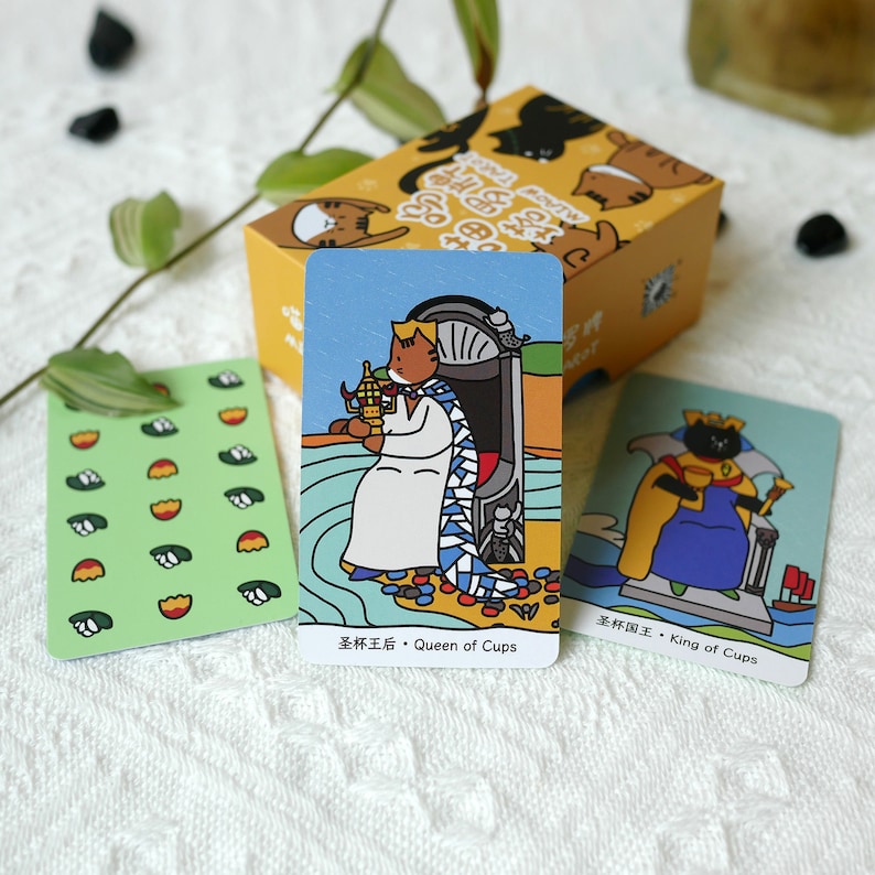 Puede incluir: Tres cartas de tarot con ilustraciones de gatos. Las cartas son de una baraja de tarot con tem&aacute;tica de gatos. Las cartas son Reina de Copas, Rey de Copas y una carta con un patr&oacute;n repetido de hojas verdes y flores naranjas.
