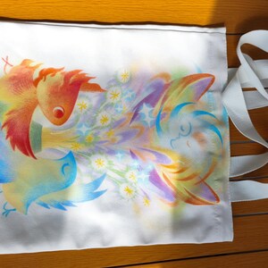 May include: White tote bag with a colorful illustration of birds and floral elements. The artwork features a bird with orange and yellow feathers, and another with blue and yellow feathers. A white strap is attached to the bag.
