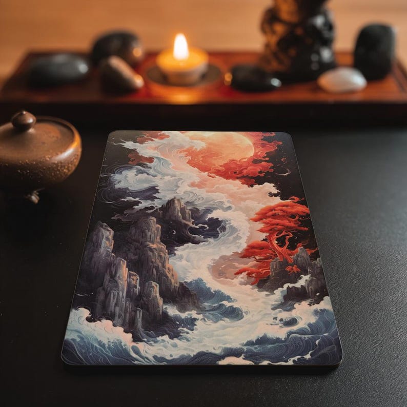 May include: A rectangular print featuring a landscape illustration with jagged dark grey mountains, swirling white and blue ocean waves, a vibrant red tree, and a large glowing orange moon set against a dark sky with clouds.