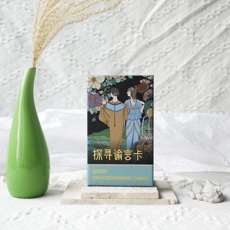 May include: A deck of cards with a blue and green floral design. The box features two women in vintage clothing and the text "Quest Enlightenment Cards" in gold lettering. The text "探索 命运 卡" is also on the box.