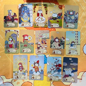 Peut inclure: Un ensemble de cartes de tarot avec des illustrations fantaisistes. Chaque carte présente une scène unique avec des personnages de dessins animés, des étoiles et des symboles. Les cartes ont une esthétique vintage avec une palette de couleurs douces de jaunes, de bleus et de bruns. Les cartes sont disposées sur une surface à motifs.
