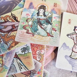 May include: A selection of illustrated cards with vibrant colours and detailed artwork. The cards depict various figures and scenes, with a focus on blues, greens, pinks, and yellows. The illustrations appear to be of Asian origin, possibly depicting mythological or historical figures.