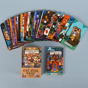 May include: A deck of "Cat Star Tales Tarot" cards with colorful illustrations of cats and other animals. The cards are fanned out, with two boxes of cards in the foreground. The boxes feature the text "Cat Star Tales Tarot".