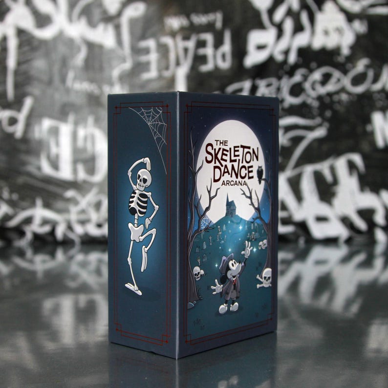 May include: A dark blue box with the text "The Skeleton Dance Arcana" and a cartoon skeleton dancing on one side. The other side features a cartoon character in a graveyard scene with a full moon. A spider web is in the corner.