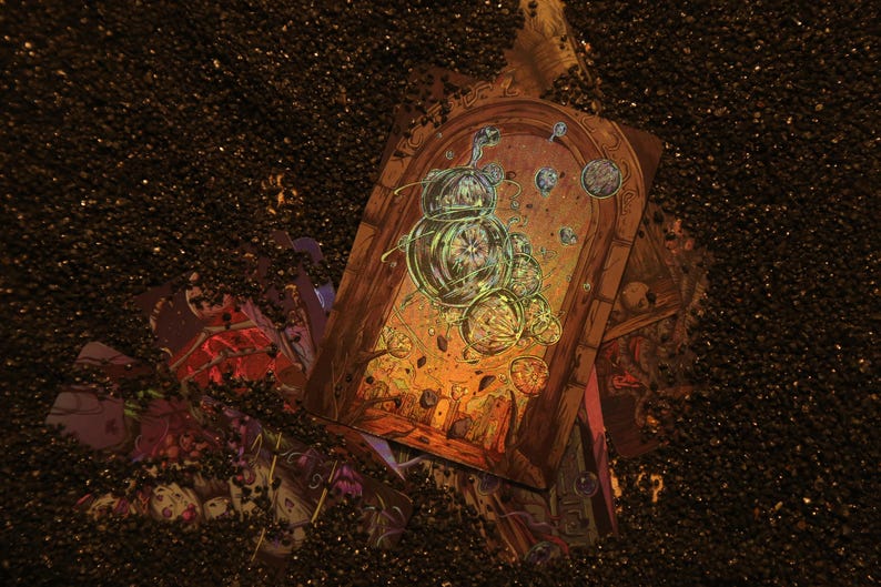 May include: A rectangular tarot card featuring a central arched doorway illustration with glowing green bubbles and celestial spheres, partially buried in dark, granular material. The artwork displays intricate line work and warm orange tones.
