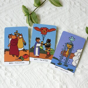 Puede incluir: Tres cartas de tarot con ilustraciones de gatos. La primera carta es el Tres de Copas, la segunda carta es el Dos de Copas y la tercera carta es el As de Copas.