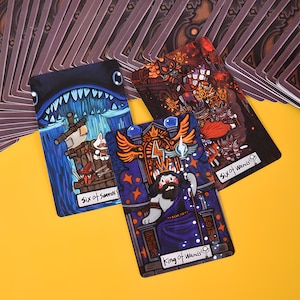 May include: Three tarot cards with colorful illustrations. The cards feature whimsical characters and scenes, including a shark, a cat-like figure, and a figure with a red cape. The cards are labeled "Six of Swords" and "King of Wands".