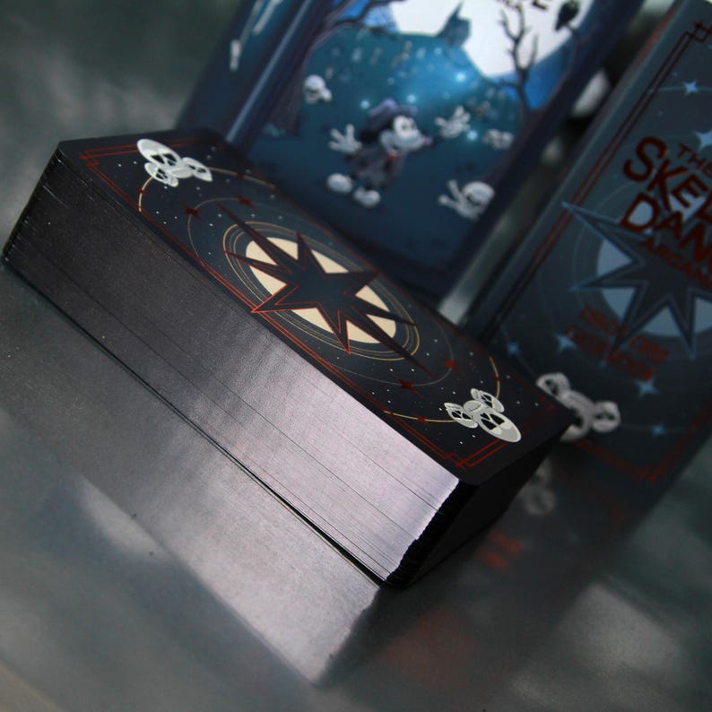 May include: A deck of cards with a dark navy blue background and a starburst design. The cards have a black edge and a red border. The deck is titled "The Skeleton Dance". The cards have a spooky theme.