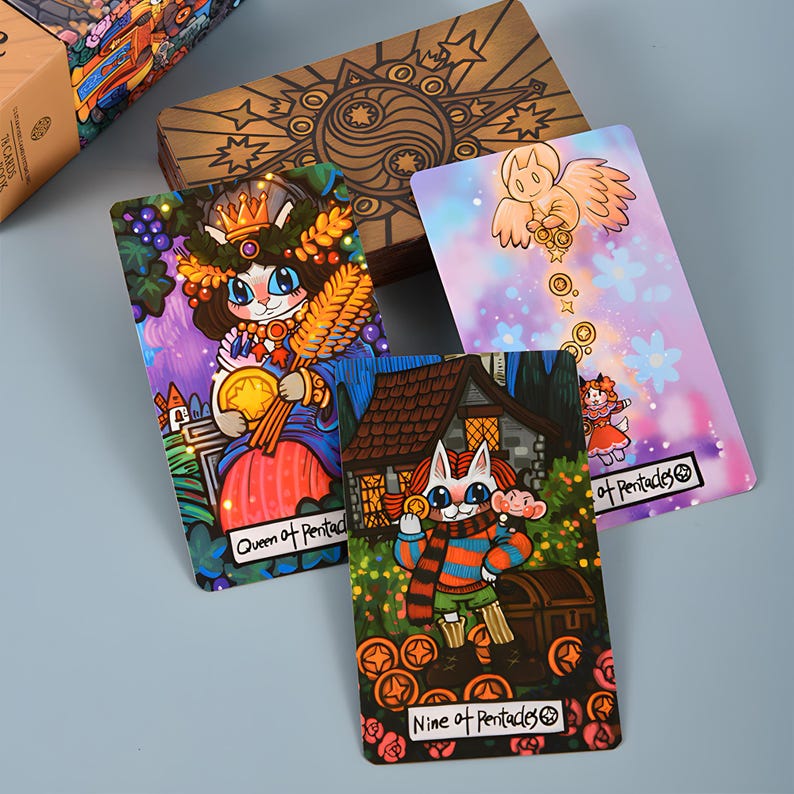 May include: A tarot card deck featuring whimsical illustrations. The cards depict anthropomorphic cats and other characters in vibrant colors. The wooden box has a yin-yang symbol and starburst design. The cards are labeled "Queen of Pentacles" and "Nine of Pentacles".
