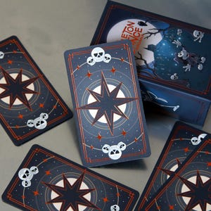 May include: A deck of tarot cards with a dark blue background, a starburst design, and skull accents. The cards are arranged around a matching box with the text "Skeleton Dance Arcana" and a spooky illustration.