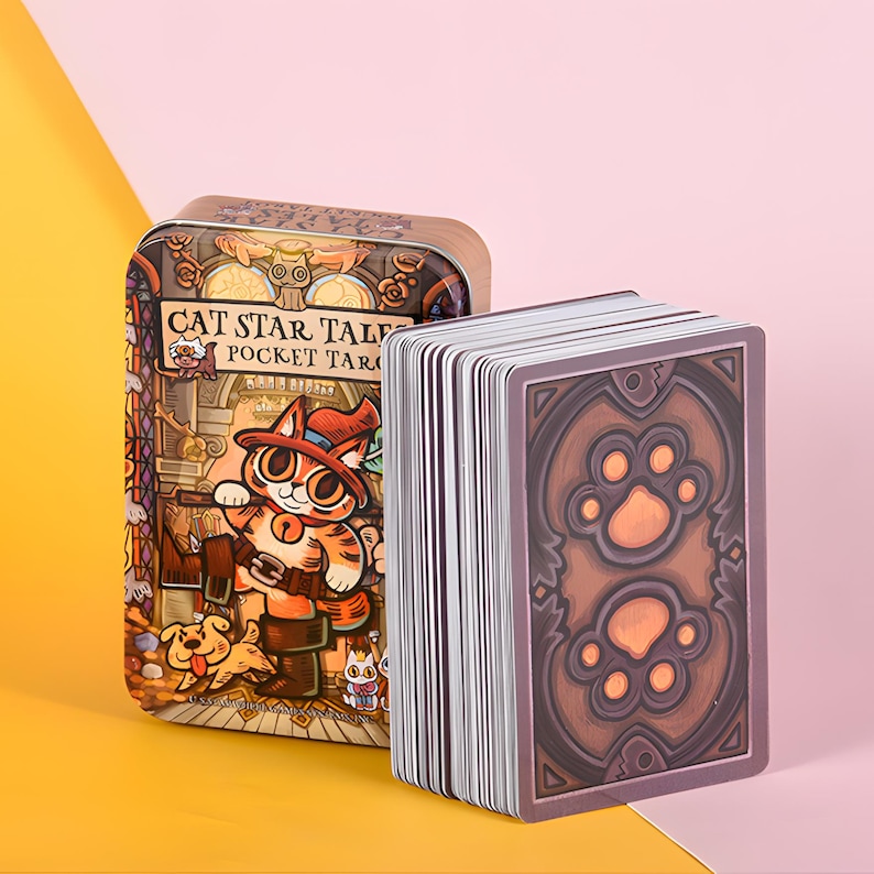 May include: A deck of tarot cards with a brown and orange paw print design on the back, next to a metal tin. The tin features a cartoon cat in a hat and the text "CAT STAR TALES POCKET TAROT". The background is pink and yellow.