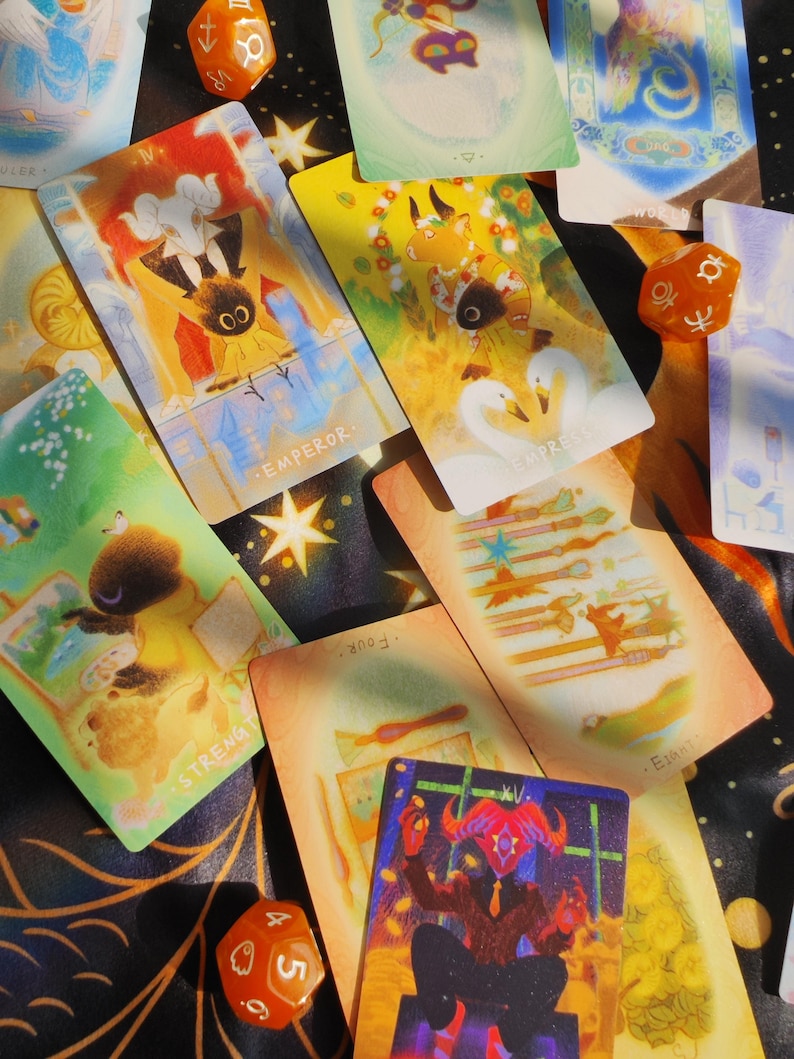 May include: A collection of tarot cards with whimsical illustrations and text, including "Emperor," "Empress," and "Strength." The cards are scattered on a dark surface, accompanied by orange dice.