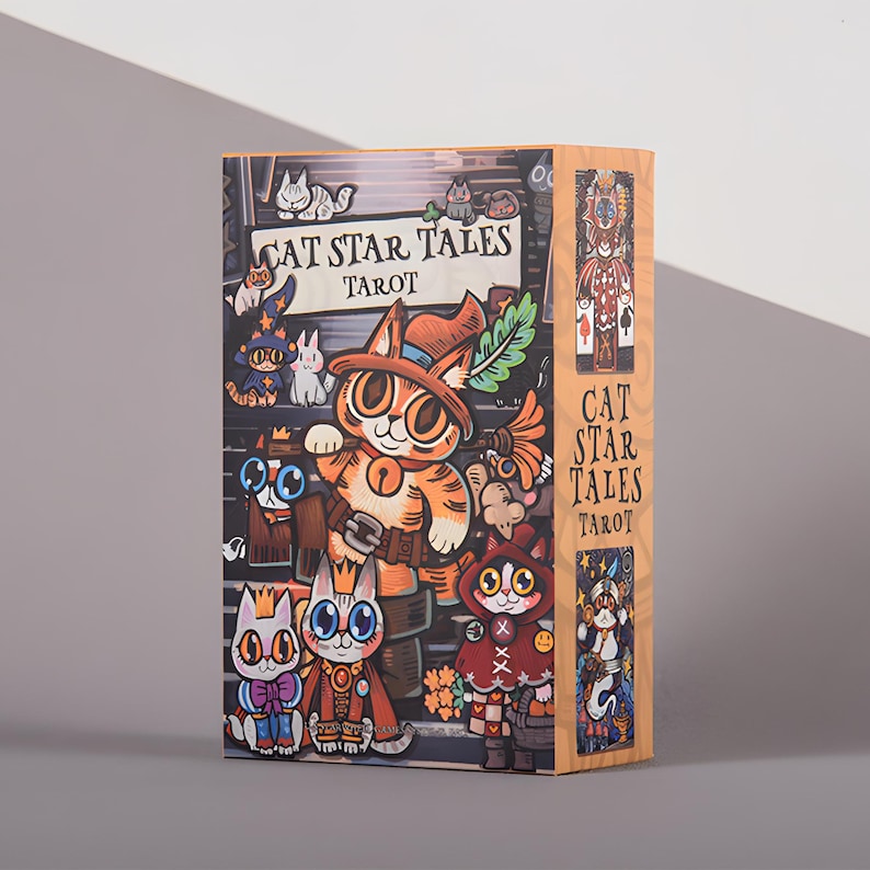 May include: A tarot card box featuring the title "CAT STAR TALES TAROT" with illustrations of cartoon cats in various costumes. The box has a light wood grain appearance and a colorful design with a whimsical theme.