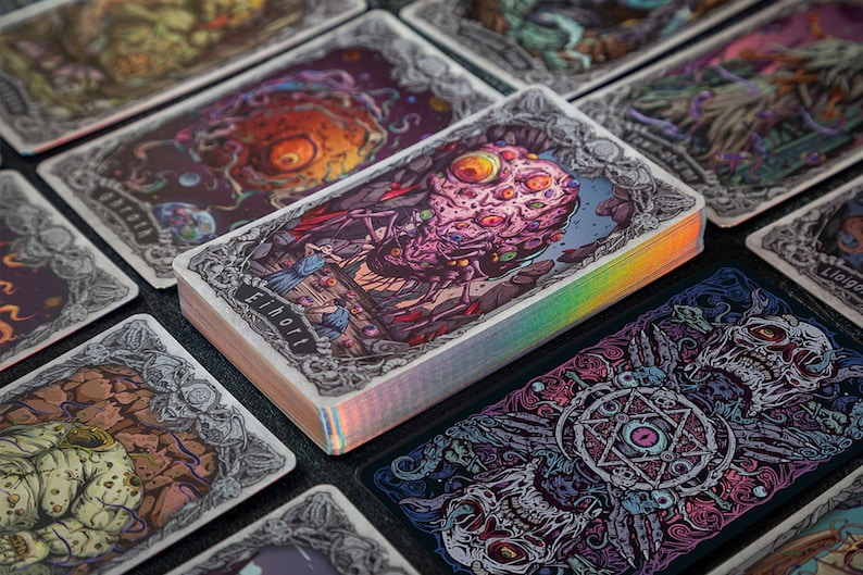 May include: A deck of rectangular playing cards with holographic edges, featuring intricate, colorful illustrations of grotesque creatures and occult symbols. The top card displays a multi-eyed, textured entity with the text Eihort printed below it.
