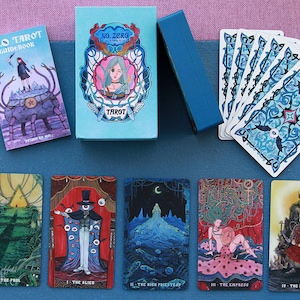 Puede incluir: Un juego de cartas de tarot No. 0 que incluye una caja azul claro con un personaje ilustrado, una guía a juego y un abanico de cartas con dorsos azules estampados. Cinco cartas de tarot individuales se muestran abajo con ilustraciones detalladas.