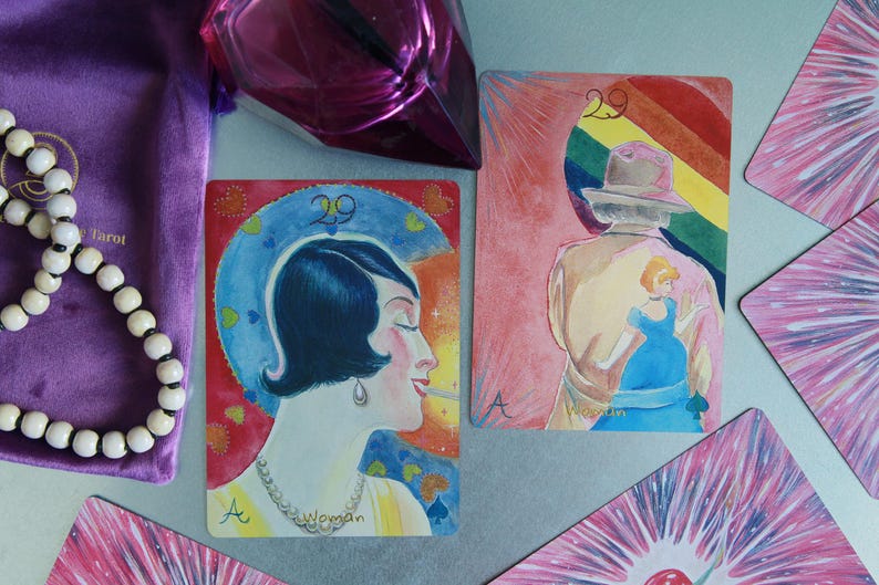 May include: Two rectangular tarot cards featuring number 29 and the letter A. One card shows a profile of a person with dark hair and a necklace. The other card depicts a person in a hat with a rainbow background and a small blue figure.