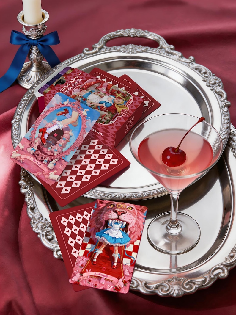 May include: A Scarlet Alice Tarot deck box and cards featuring illustrations of a character in a blue dress, a martini glass with a cherry, and a silver tray. The cards display the text Scarlet Alice Tarot Deck, The Fool, and Strength.