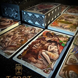 May include: A tarot card deck with decorative card boxes and individual cards. The cards feature detailed illustrations with gold accents. The word "STRENGTH" is visible on one card. The text "TAROT THE FOREST KNOWS" is at the bottom.